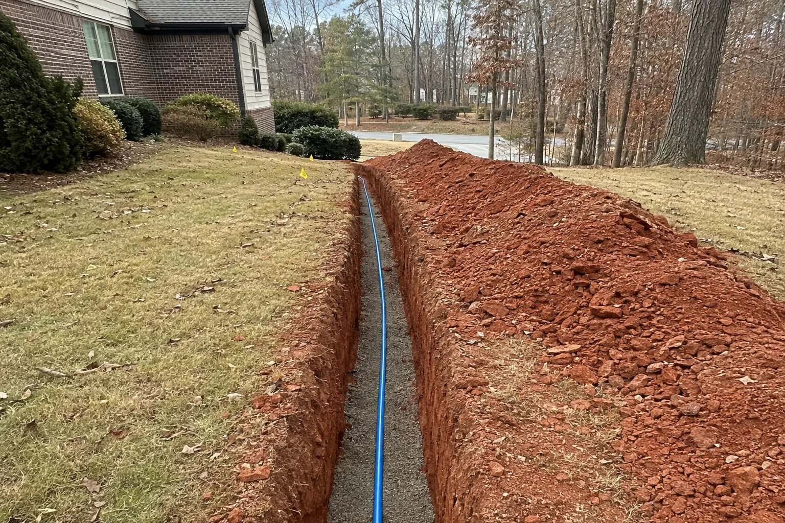 Blue potable-water tube laid continuously on bedding in a narrow residential trench